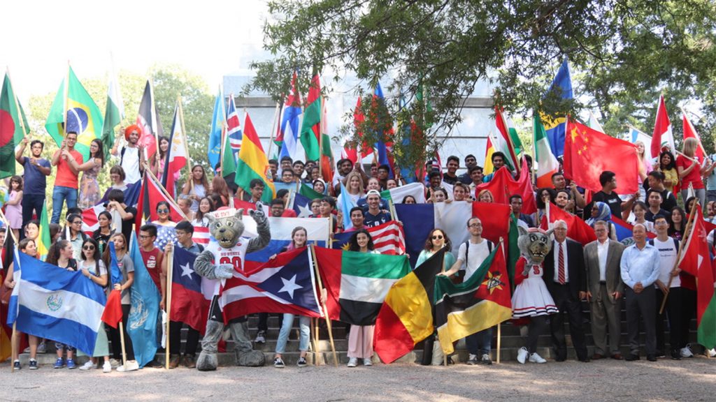 Students with flags from around the world in front of the belltower with Mr. and Ms. Wuf and the Chancellor.
