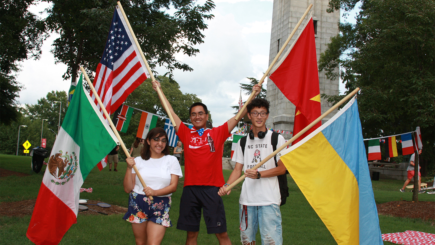International students holding their country's flags in front of the belltower.